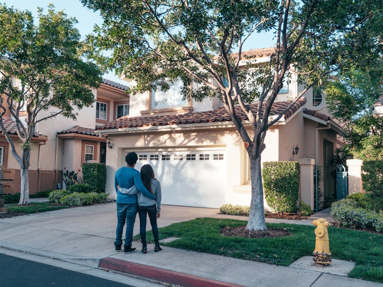 Couple hugging outside their newly purchased suburban home, showcasing togetherness and new beginnings. Stillwater Real Estate agents
